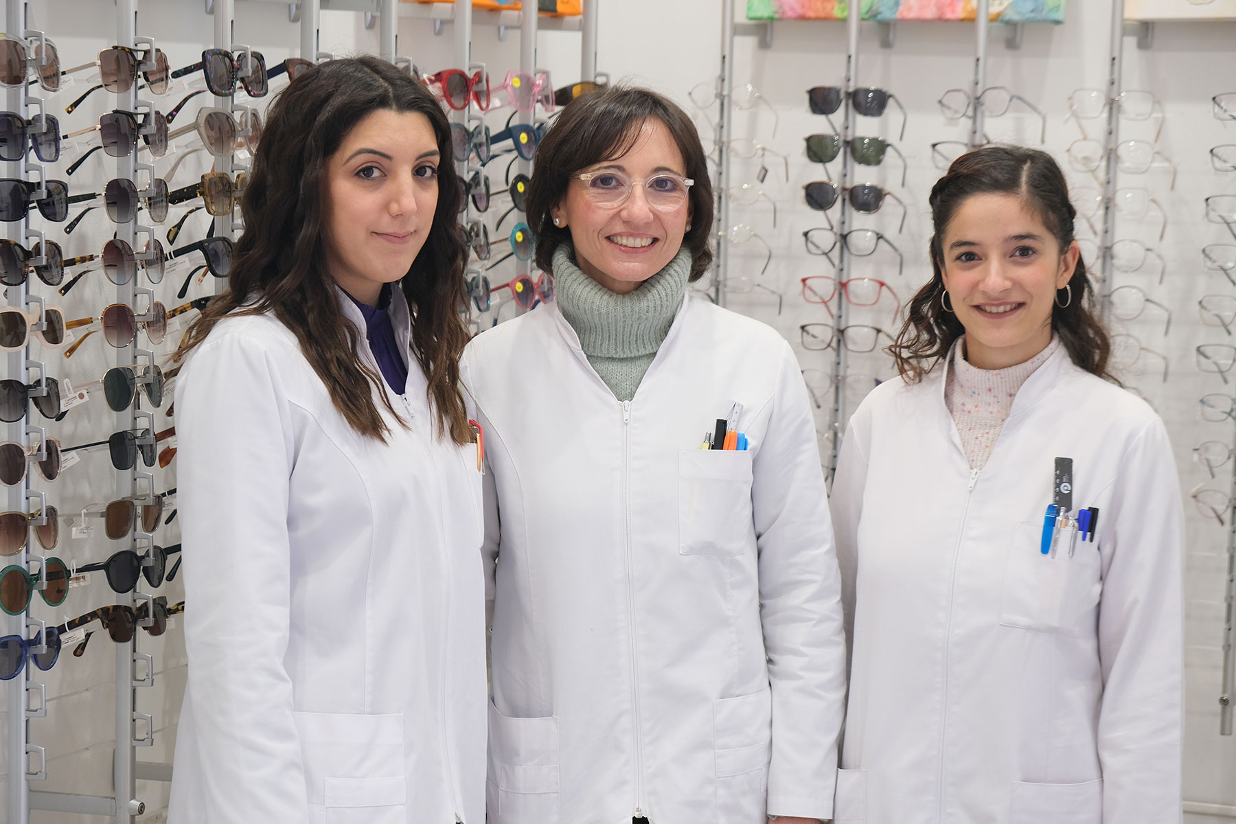 Noemí, Nerea y Lorena (personal de la óptica) posando frente a un stand lleno de modelos de gafas.